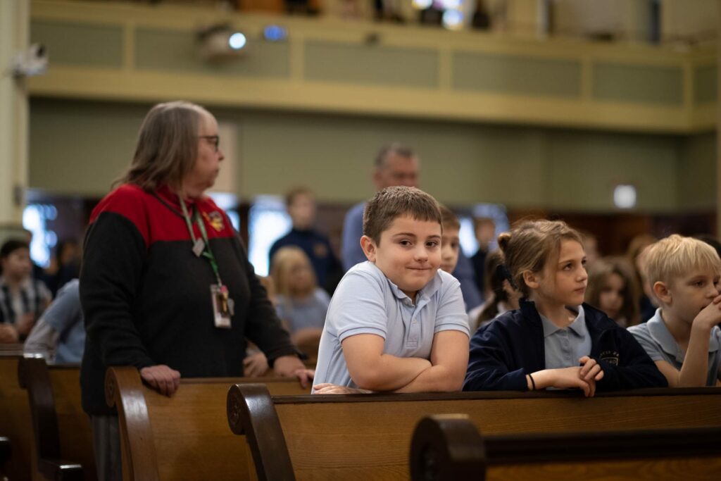 Kids wearing uniforms in pews in a church.