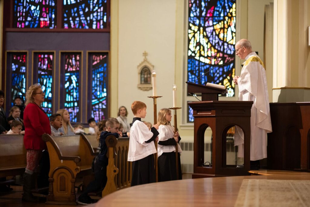 The preacher looking down at two kids holding candles.