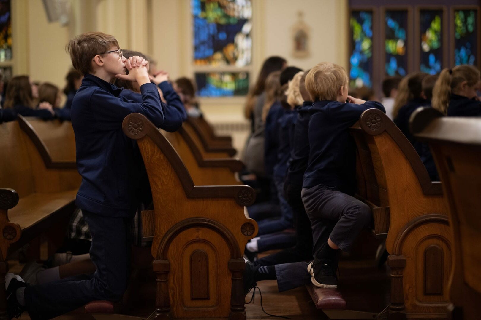 Group of boys kneeling in pews in a church.