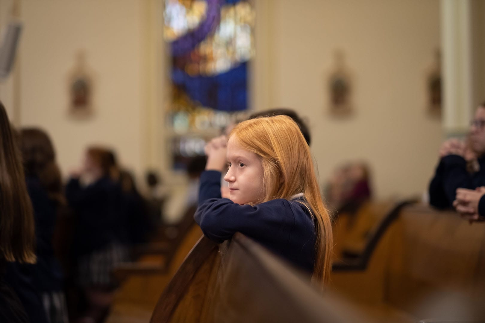 Little girl leaning over a pew in a church.