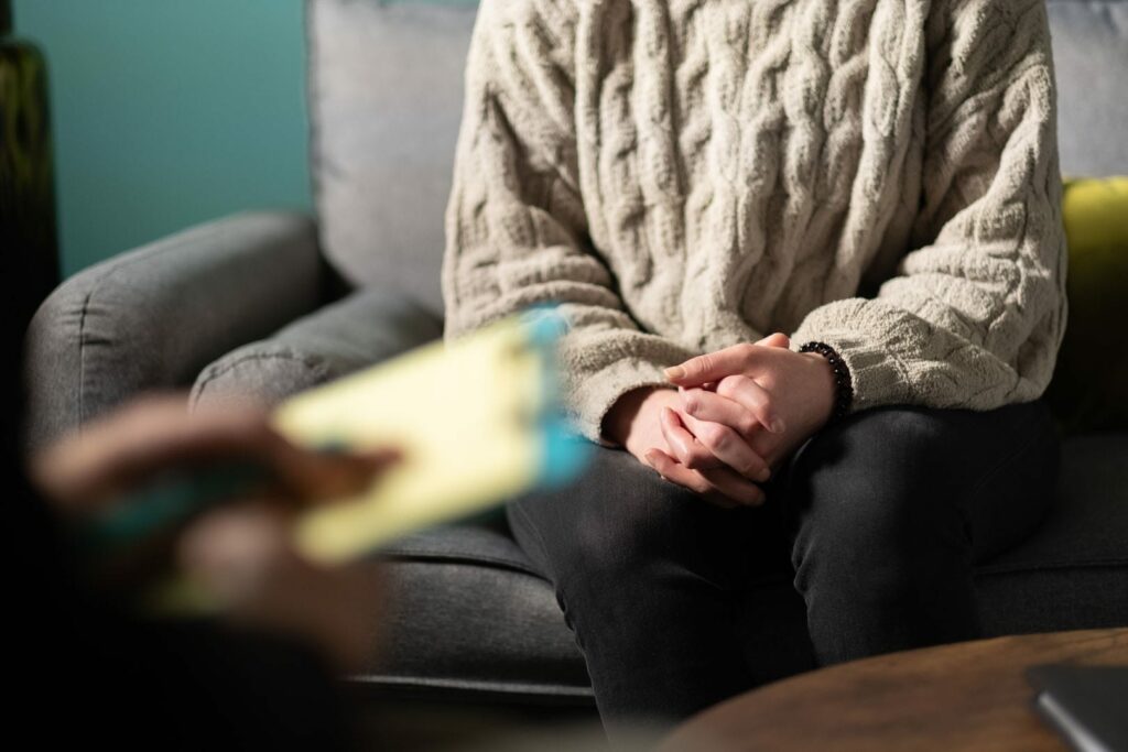 A person sitting on a couch with clasped hands.