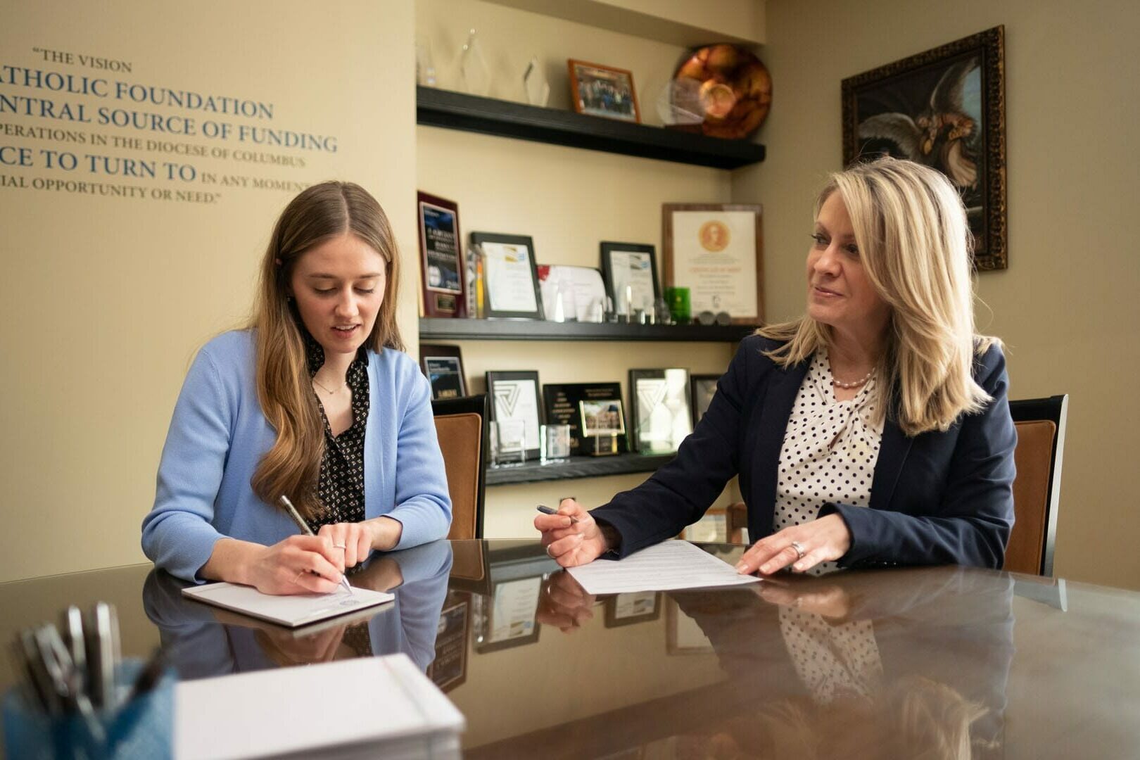 Two women signing documents at a table.