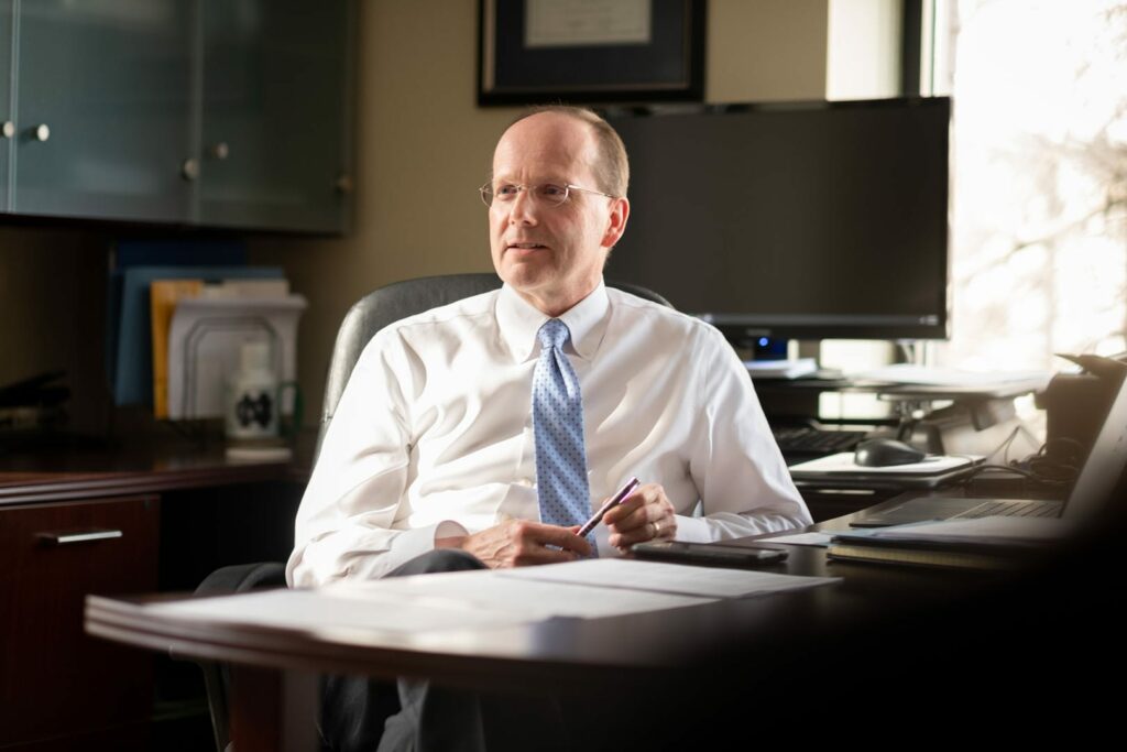 An older man in a white shirt at a desk.