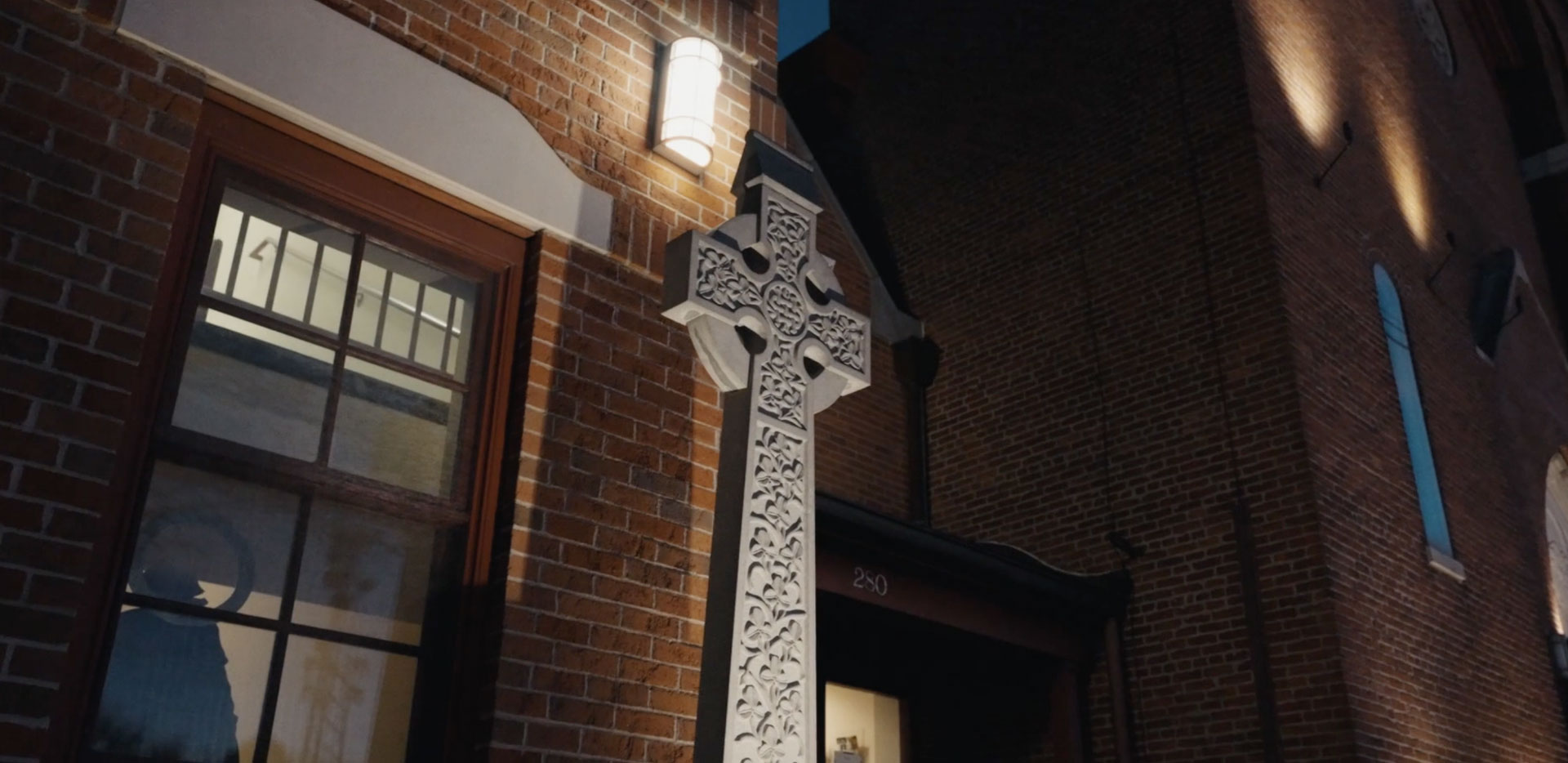 Dramatically lit church with stone cross in the foreground.