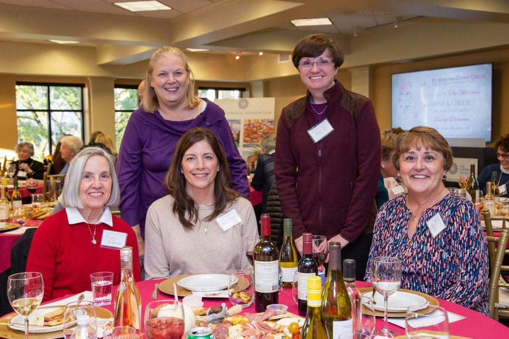 Women standing and sitting around a table dining at an event.