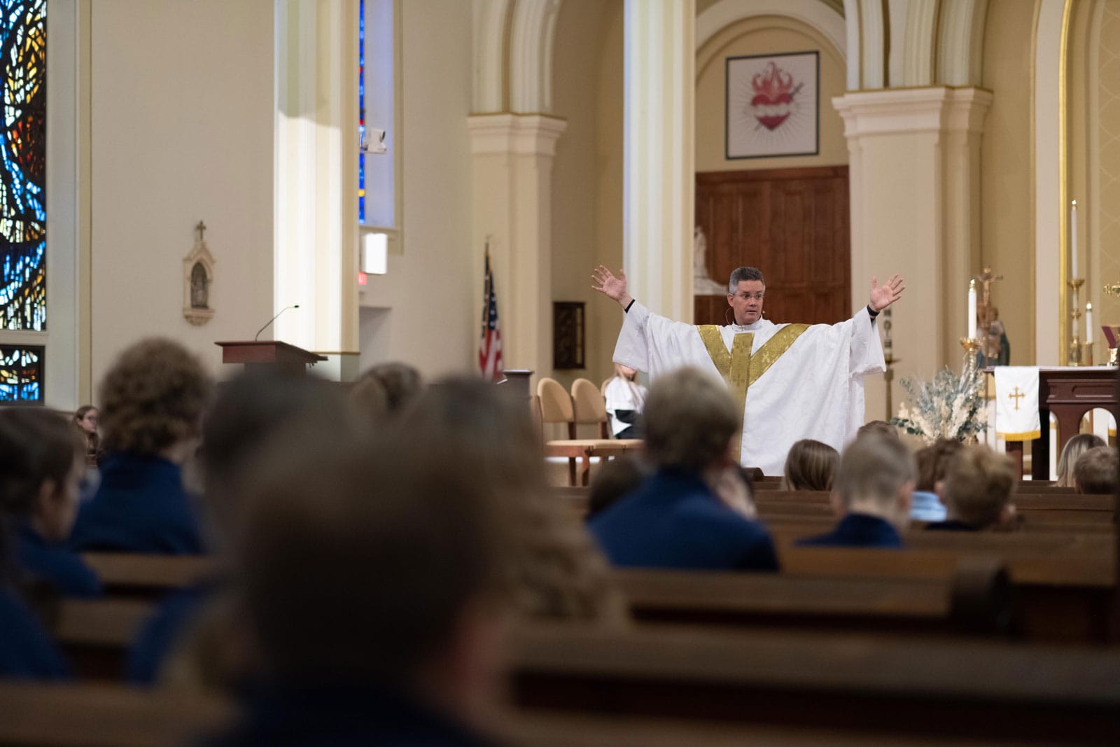 Man with hands raised giving sermon at a church adorned in white and gold clothes.