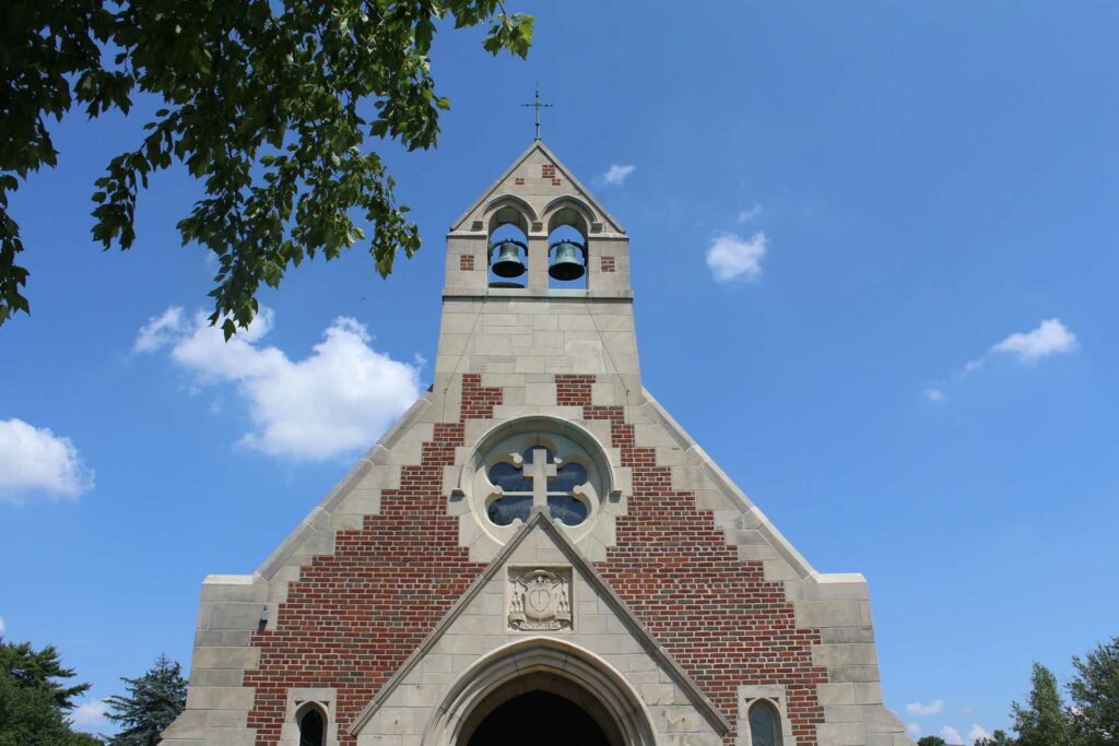 Church bells atop a brick church with decorative windows.