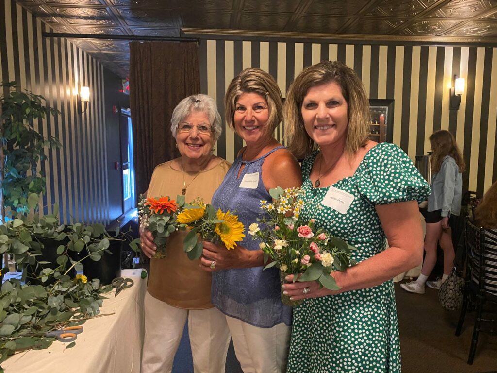 Three women smiling and holding flowers.