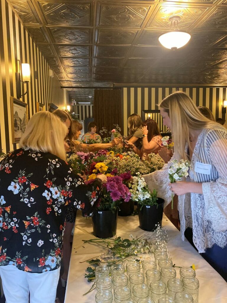 Women exploring various bouquets of flowers on a long table.