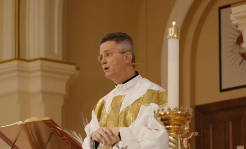 Man in white and gold robes giving sermon.