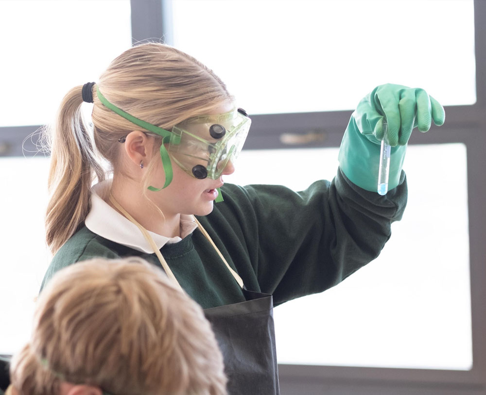 Young blonde woman inspecting a test tube with safety goggles.